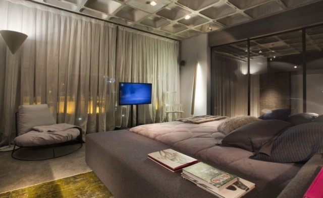 chambre-coucher-moderne-grise-élégante-rideaux-gris-clair-légers-fauteuil-élégant-tv-écran-plasma