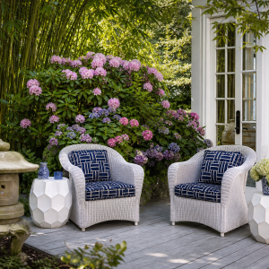 Terrasse extérieure élégante avec fauteuils en rotin blanc, coussins bleu marine et jardin verdoyant