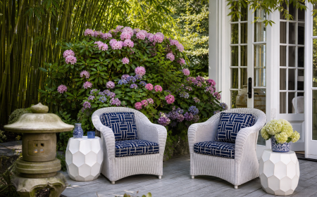 Terrasse extérieure élégante avec fauteuils en rotin blanc, coussins bleu marine et jardin verdoyant