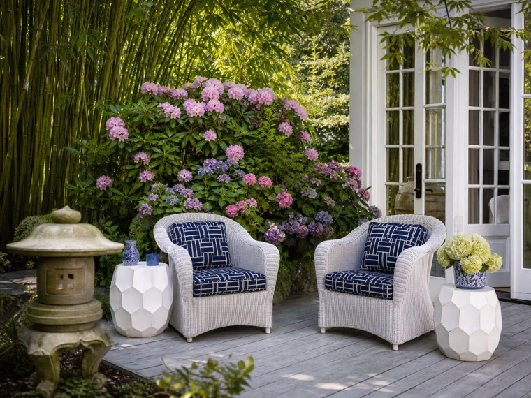 Terrasse extérieure élégante avec fauteuils en rotin blanc, coussins bleu marine et jardin verdoyant