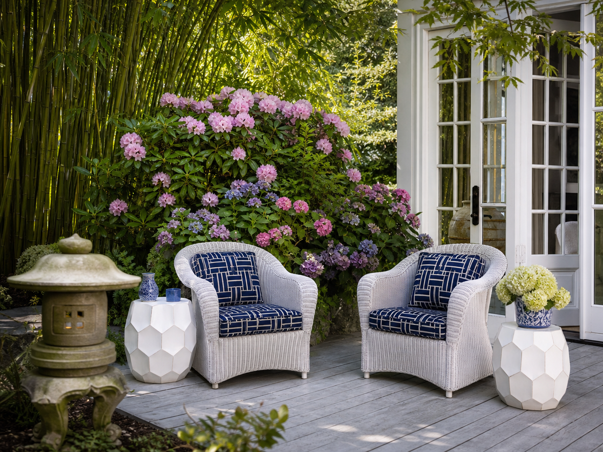 Terrasse extérieure élégante avec fauteuils en rotin blanc, coussins bleu marine et jardin verdoyant