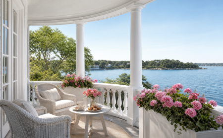 Bacs à fleurs blancs en bois sur véranda côtière avec vue mer et géraniums roses