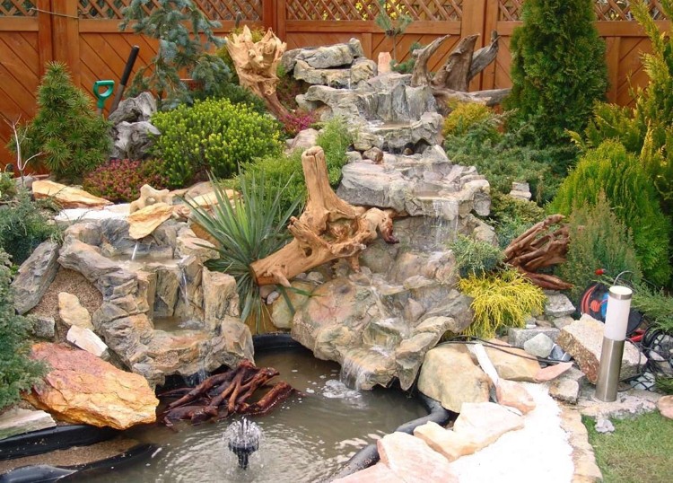 cascade de bassin décorative en pierre naturelle décorée d'arbustes conifères et de plantes vivaces cascade bassin de jardin -pierre-naturelle-arbustes-conifères-vivaces-bois-flotté