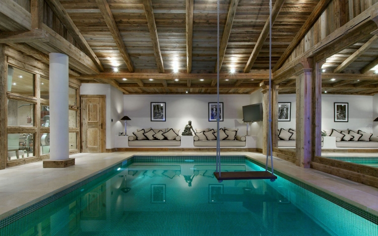 grande-piscine-intérieure-plafond-bois-massif-canapés-coussins