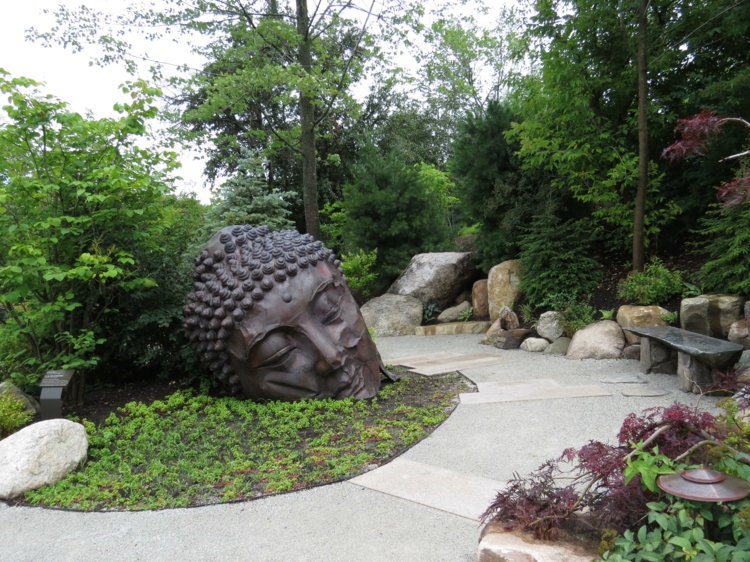 jardin asiatique statue-bouddha-tête-métal-allée-grosses-pierres-banc