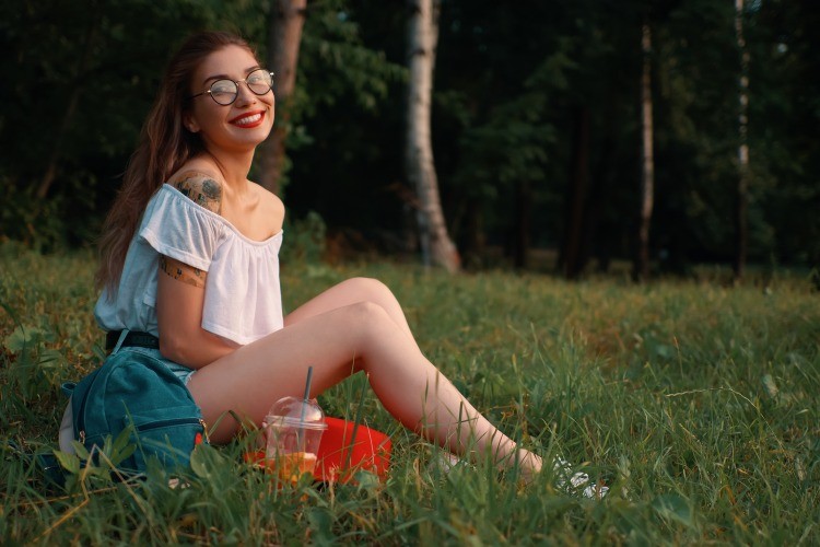 jeune fille souriante assise sur herbe dans la nature sous le soleil