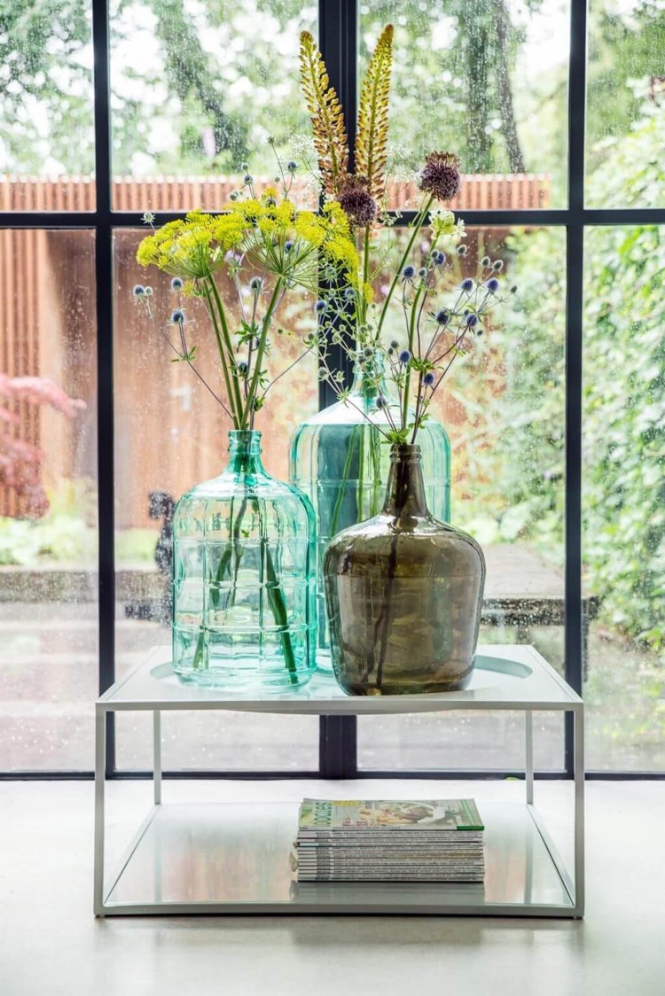 accumulation vases dame jeanne verre colore compositions florales table basse blanche