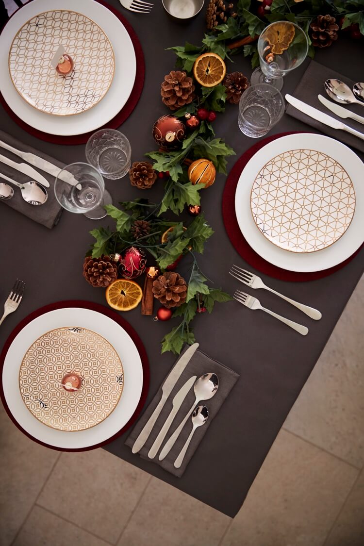 table de Noel elegante assiettes decoratives centre de table guirlande verdure pommes de pin
