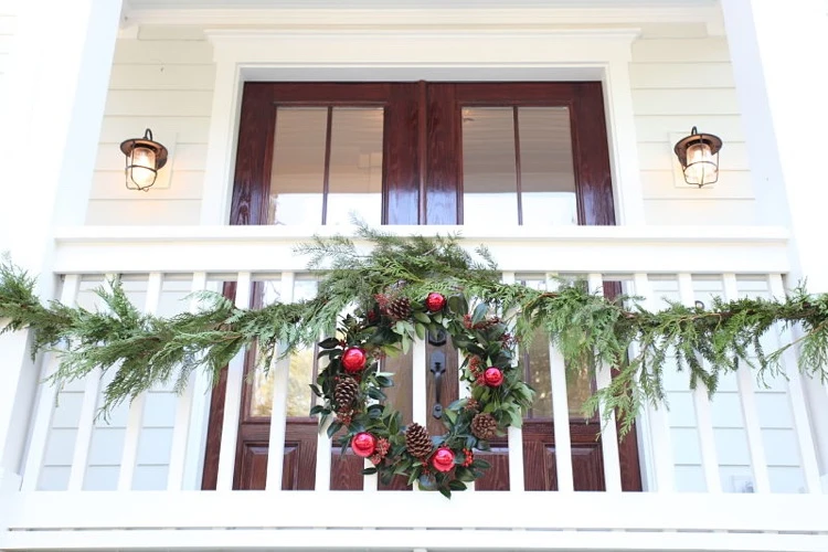 comment décorer un petit balcon pour Noel branches de cyprès couronne de Noel verdure pommes de pin et boules rouges