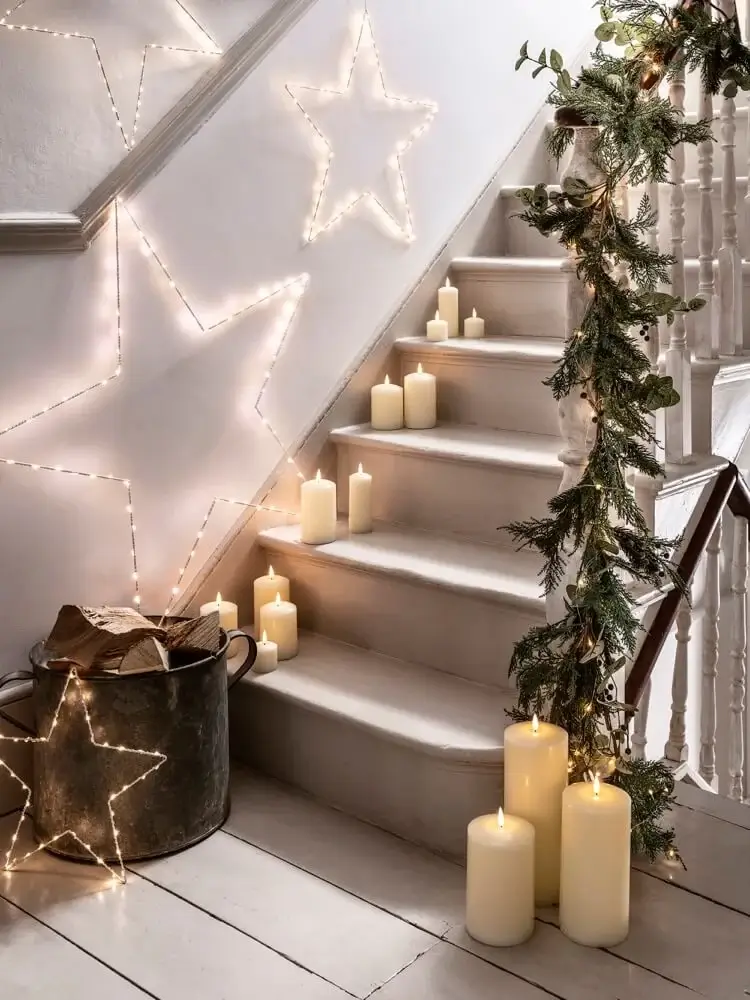 guirlande de sapin étoiles lumineuses et beaucoup de bougies cylindriques sur les marches de l escalier scandinave