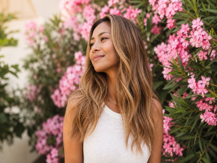 Femme aux cheveux blond caramel devant des fleurs roses en automne