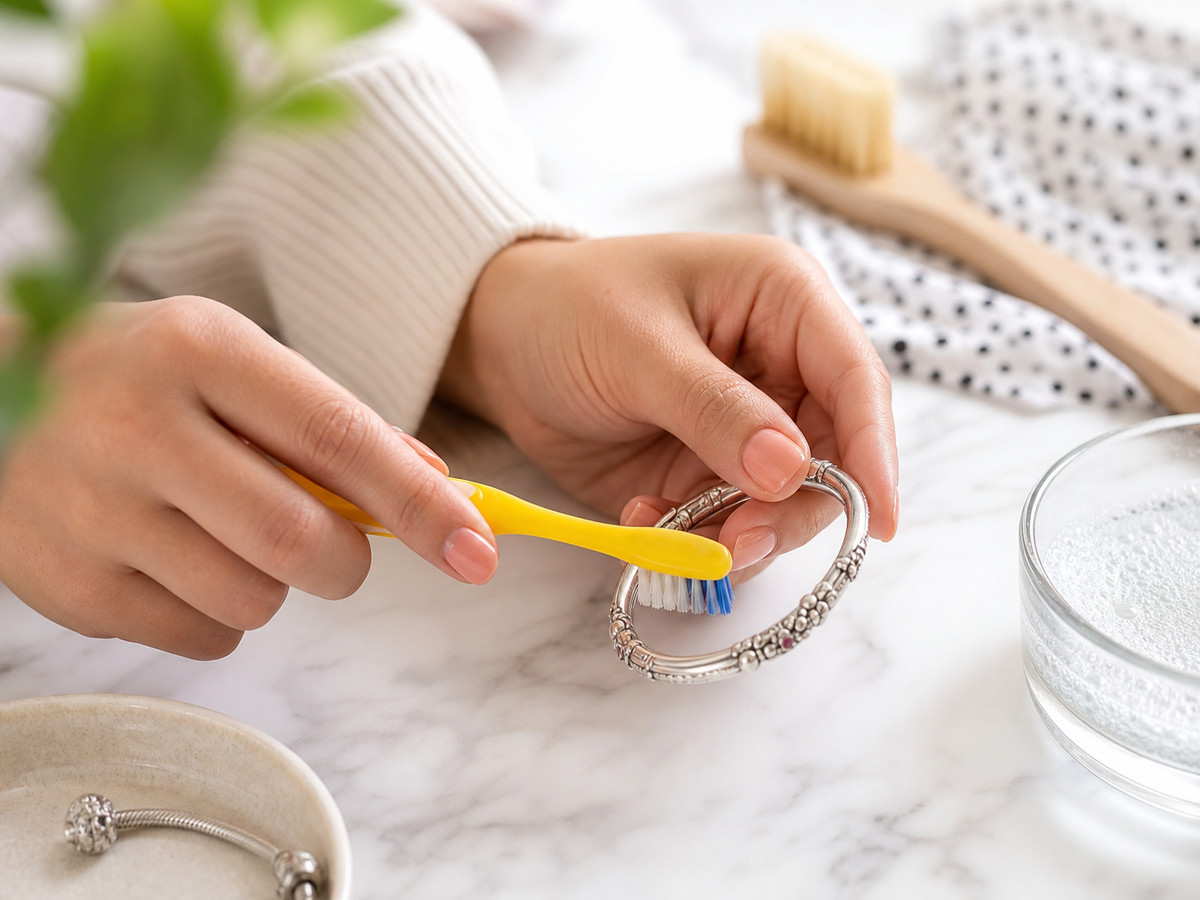Mains nettoyant un bracelet en argent avec une brosse à dents et du dentifrice blanc