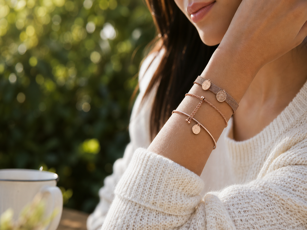 Poignet portant des bracelets empilés en or rose avec charms ronds sur fond de feuillage vert