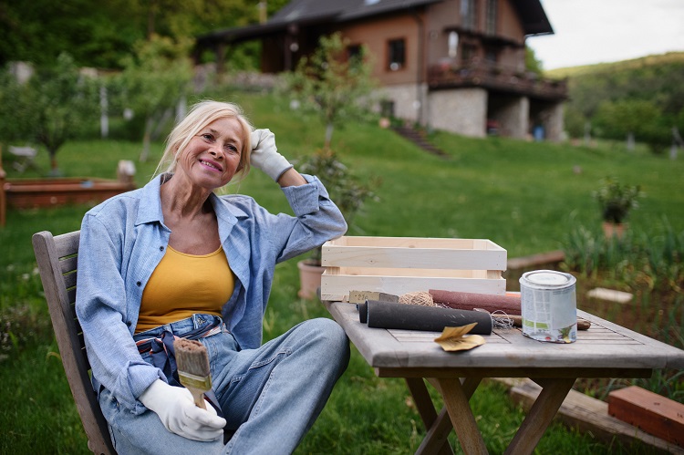 happy senior woman sitting and resting while doing paint craft outdoors in garden.