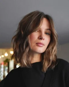 les cheveux courts et légèrement ondulés mettent en valeur la frange rideau