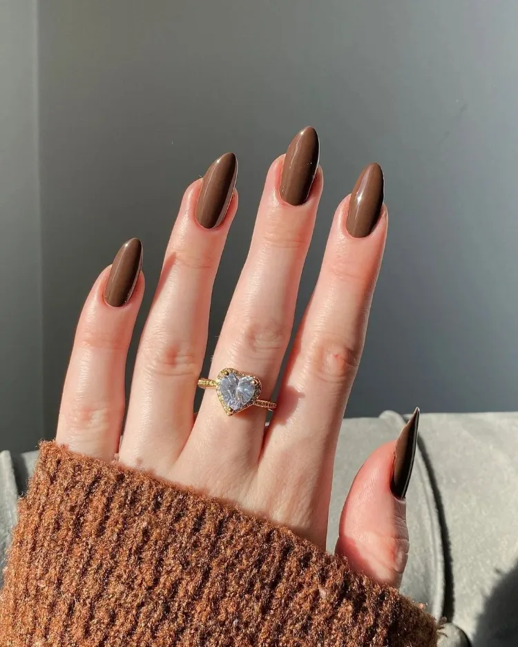 du vernis marron foncé sur des ongles en amande