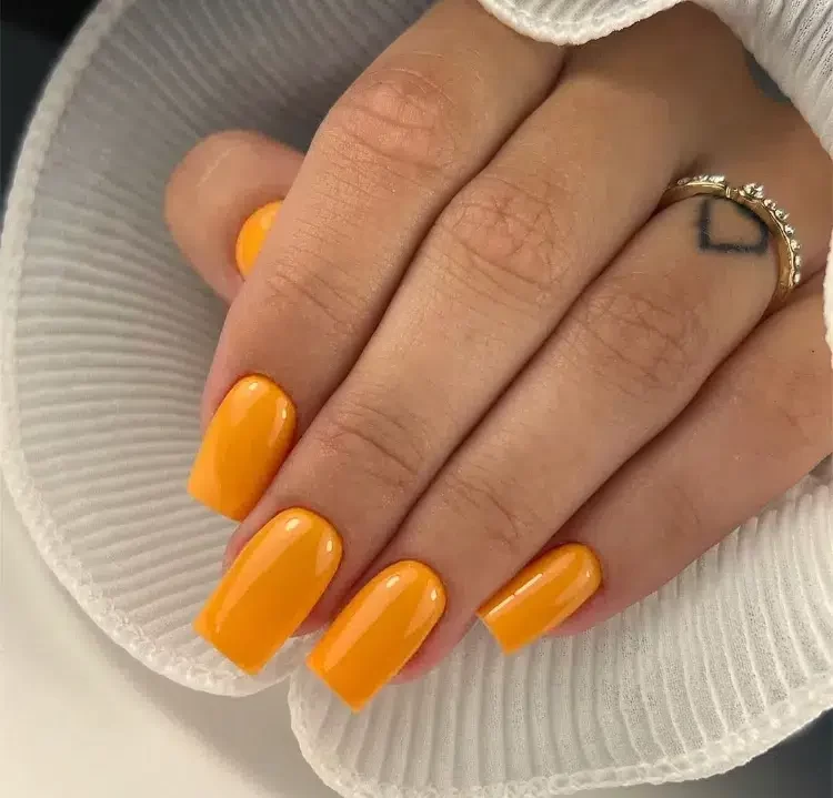 une manucure en orange vif sur des ongles longs carrés