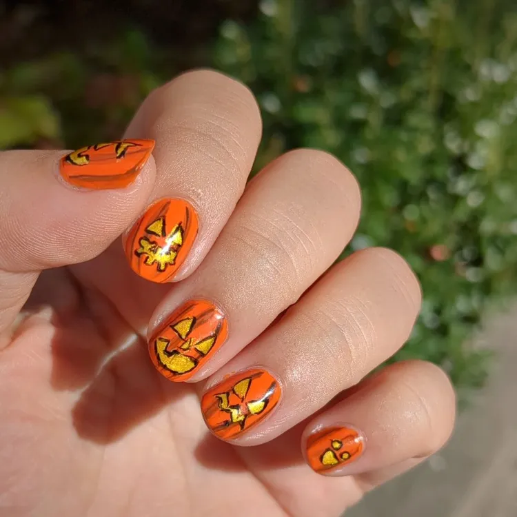 une manucure d'halloween en orange avec le motif de jack o' lantern sur des ongles courts