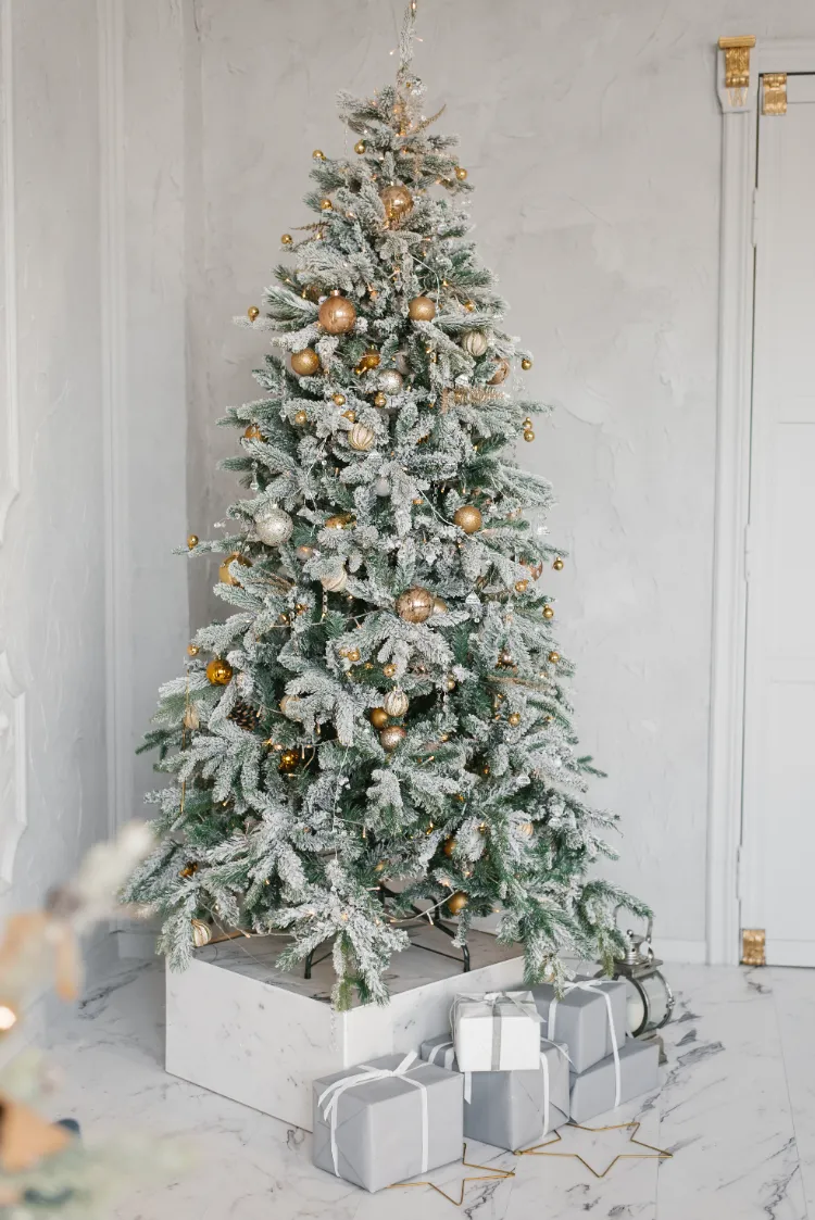 sapin de noël floqué décoré de boules dorées petites et grandes pommes de pin et guirlandes lumineuses