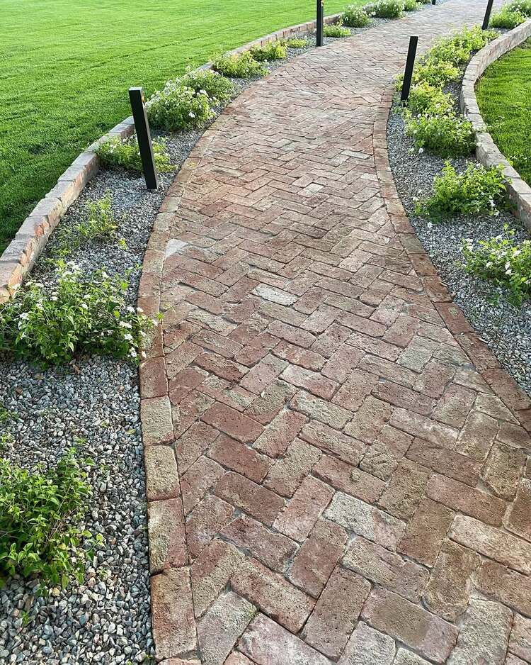 une allée en briques à motif chevron encadrée de gravier et de verdure