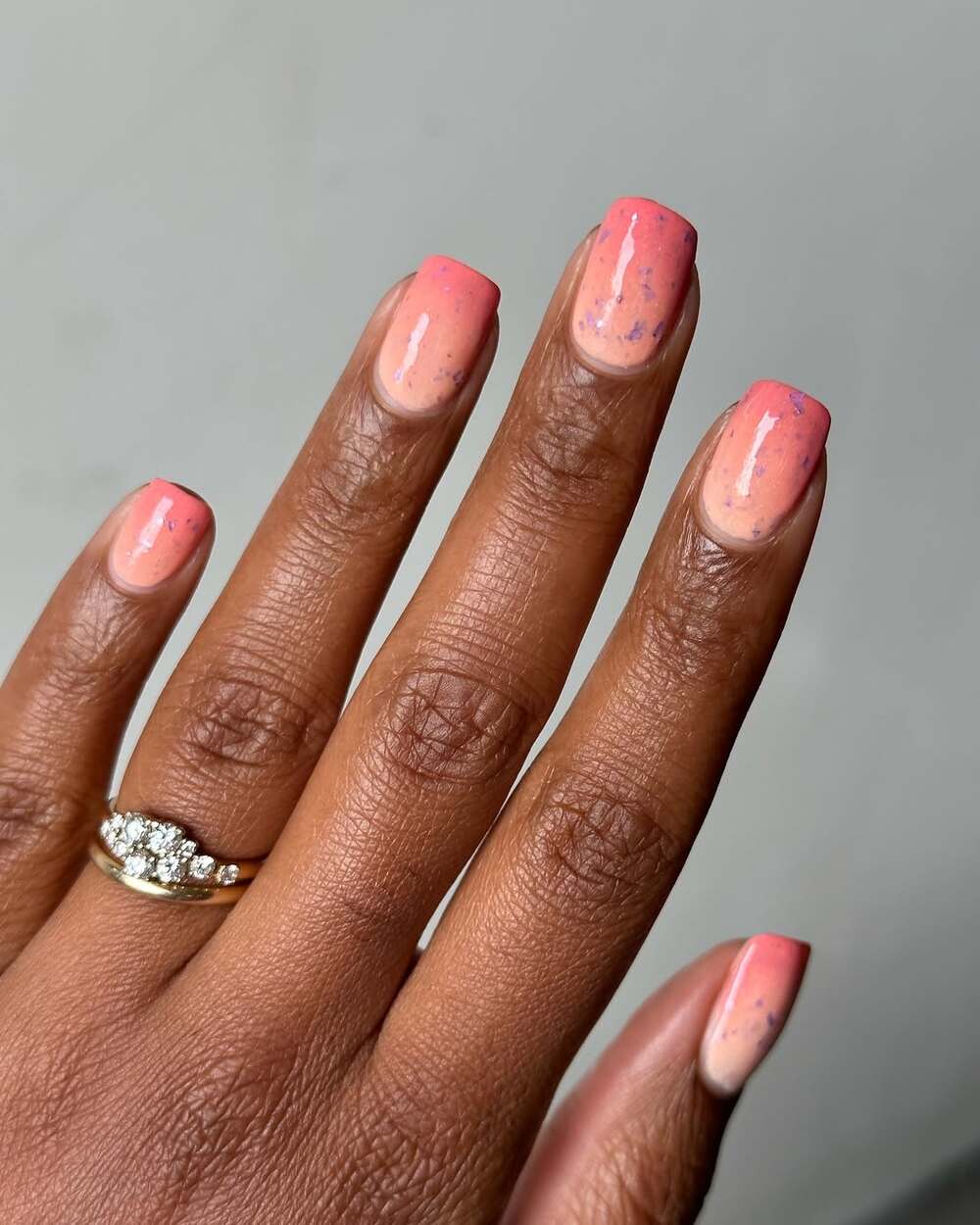 Ongles courts en carré ornés d’un dégradé pêche et rose avec de légers éclats violets - un look frais et discret pour l’été