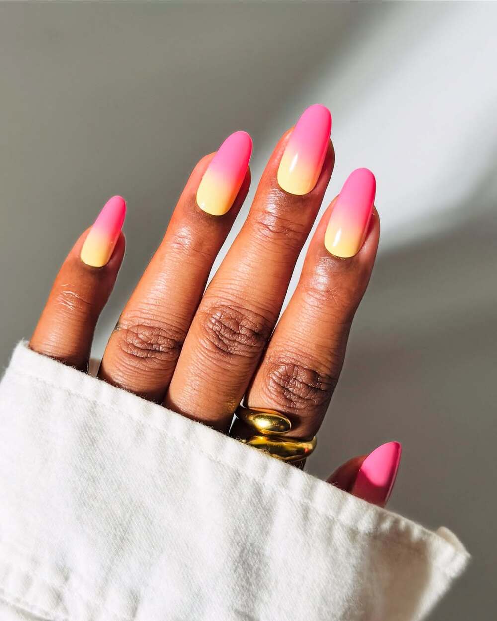 Une manucure en dégradé rose et jaune pastel néon, évoquant un cocktail tropical, parfaite pour illuminer vos journées d’été