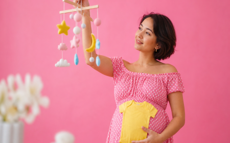 Femme enceinte tenant un mobile bébé et une grenouillère jaune, calendrier chinois de grossesse