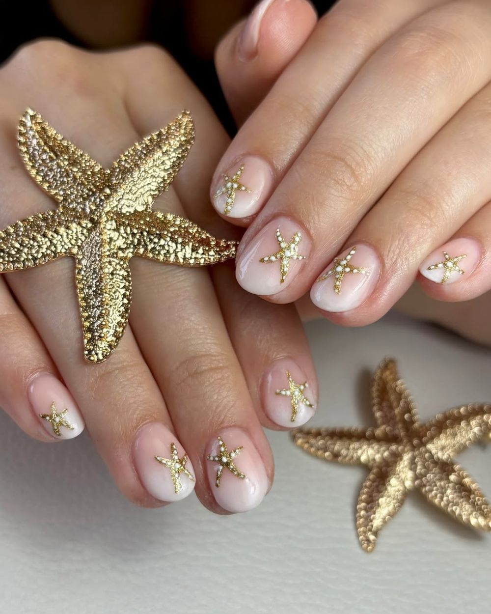 ongles courts nude sublimés par un nail art étoiles de mer dorées