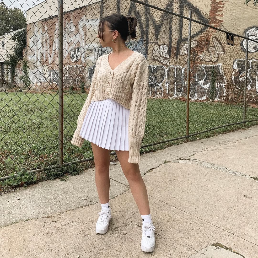 associer un gilet court en maille torsadée à une jupe plissée blanche pour créer un look universitaire cool pour la rentrée
