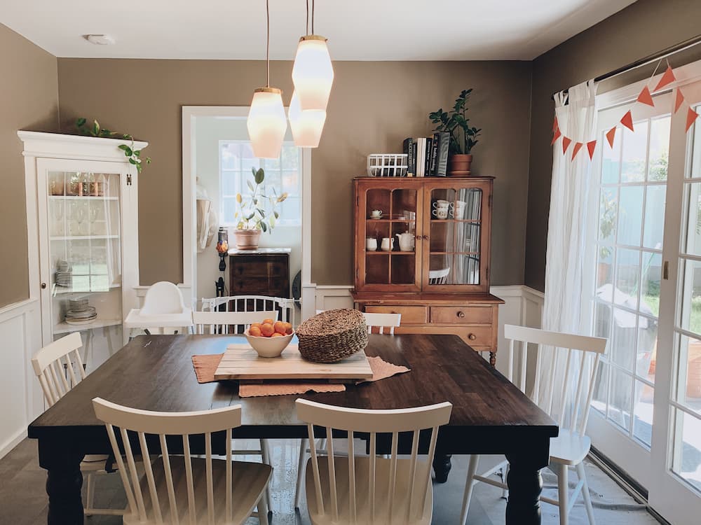 salle à manger chaleureuse rustique moderne grande table en bois sombre entourée de chaises blanches vitrine en bois avec vaisselle et plantes