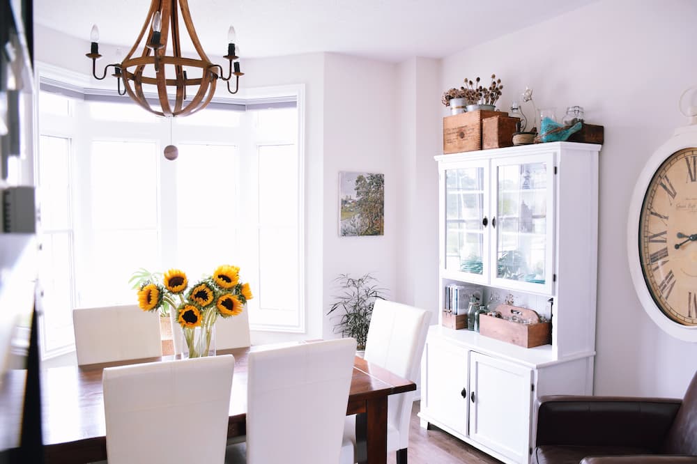 salle à manger rustique chic table en bois entourée de chaises blanches horloge murale vintage vaisselier blanc avec portes vitrées fauteuil en cuir brun