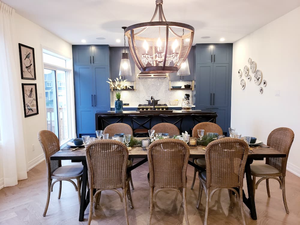 salle à manger style ferme moderne grande table en bois entourée de huit chaises en rotin lustre en métal et bois armoires bleu foncé îlot noir tabourets hauts