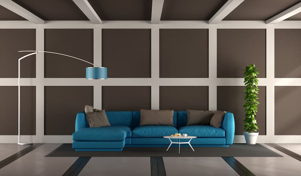 salon grand canapé bleu vif coussins gris lampe arc table basse ronde mur géométrique marron chocolat et blanc