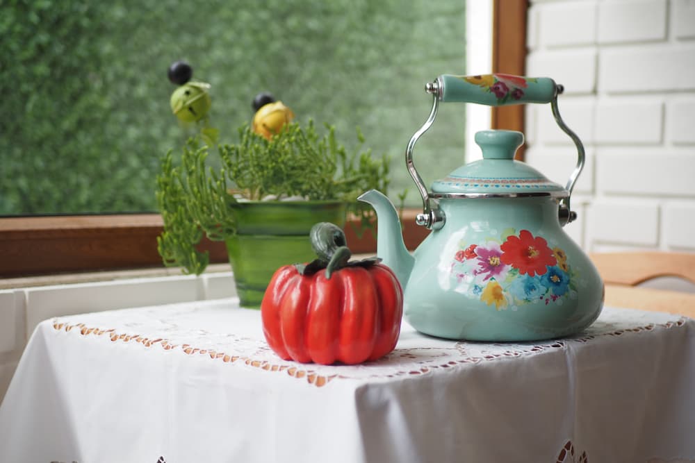 bouilloire fleurie verte et citrouille décorative sur table près d’une fenêtre