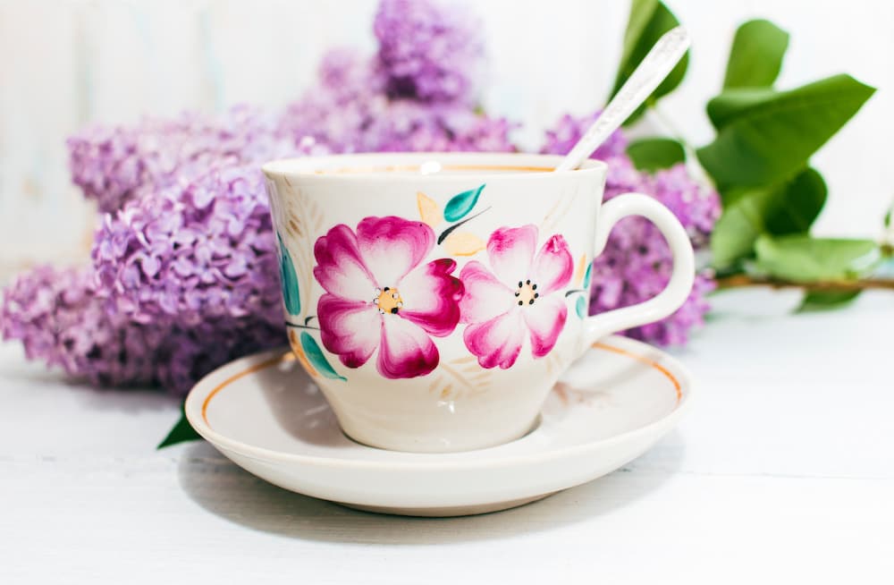 tasse fleurie avec cuillère sur soucoupe devant des fleurs violettes, ambiance printanière