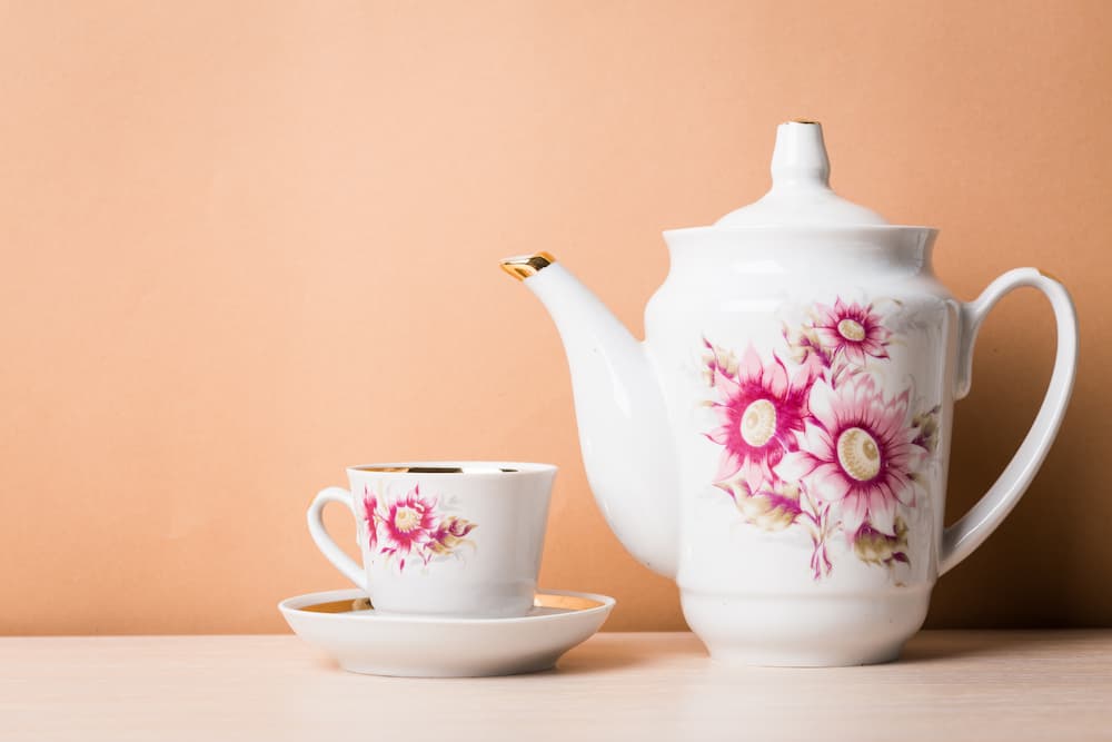 théière et tasse blanches décorées de fleurs roses posées sur table