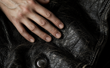 Veste en simili cuir qui s'effrite — gros plan sur texture craquelée avec une main posée dessus