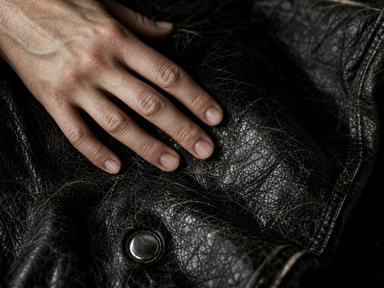 Veste en simili cuir qui s'effrite — gros plan sur texture craquelée avec une main posée dessus