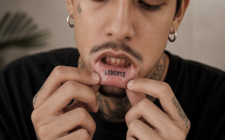 Homme montrant son tatouage intérieur de lèvre avec lettres noires en tirant sur sa lèvre inférieure