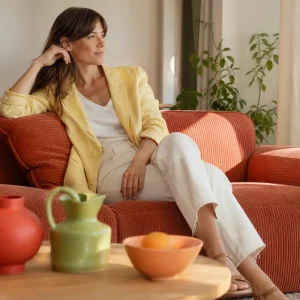 Salon français lumineux avec canapé terracotta, blazer en lin jaune beurre et accessoires vert pistache et rouge tomate