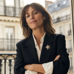 Femme en blazer oversize noir portant une broche dorée étoile au revers, terrasse parisienne en arrière-plan