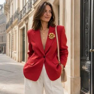 Femme en blazer oversize rouge et pantalon blanc avec broche XXL dans une rue parisienne