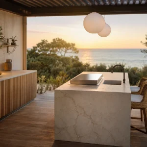 Cuisine extérieure avec plan de travail en céramique grand format sable veiné et îlot central avec plancha sur terrasse bois