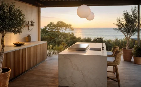 Cuisine extérieure avec plan de travail en céramique grand format sable veiné et îlot central avec plancha sur terrasse bois