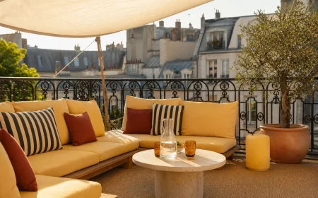 Terrasse parisienne aménagée comme un salon d'hôtel avec canapé bas, coussins jaune beurre et lampe nomade au coucher du soleil