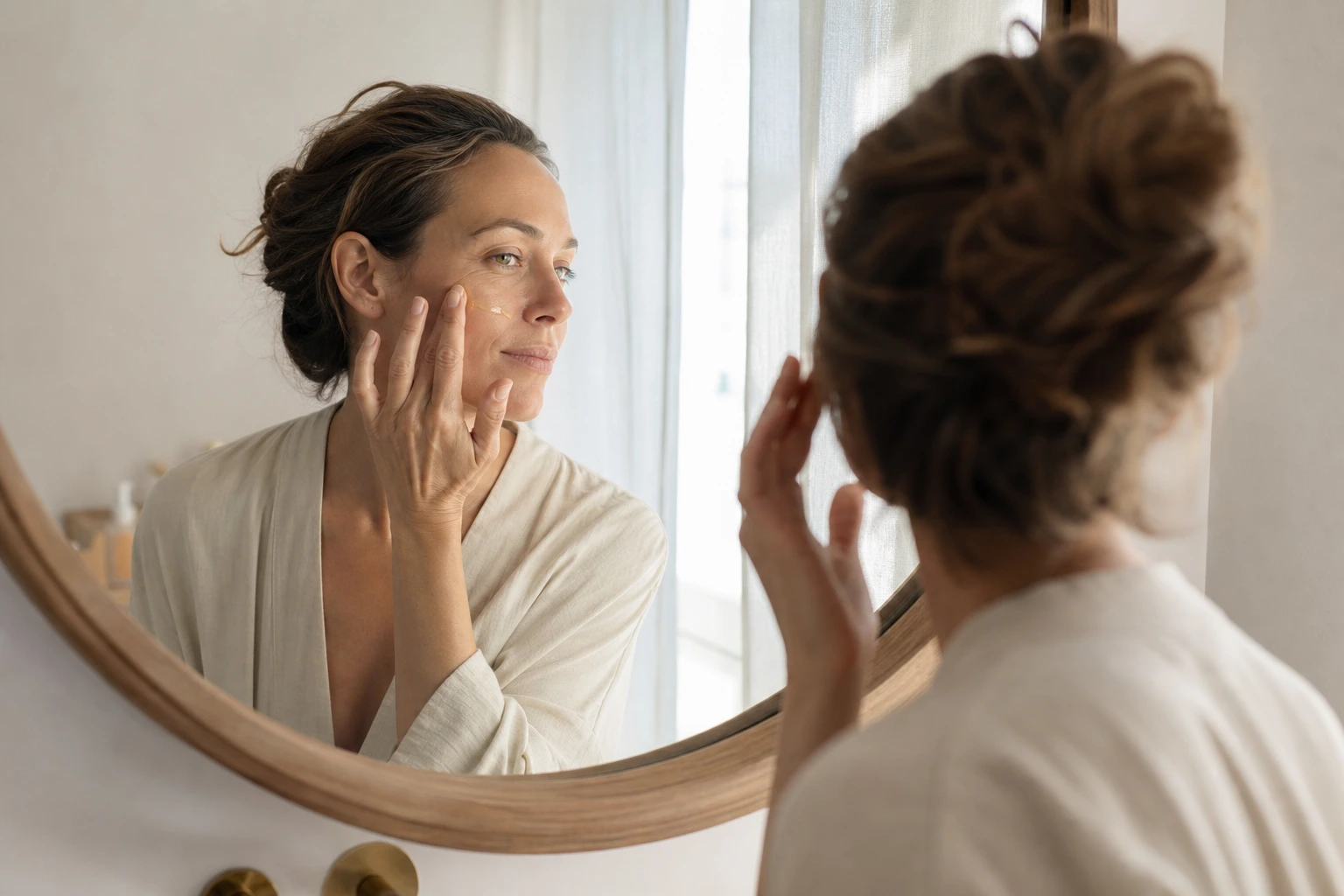 Femme appliquant un sérum antioxydant sur sa joue le matin devant un miroir de salle de bains