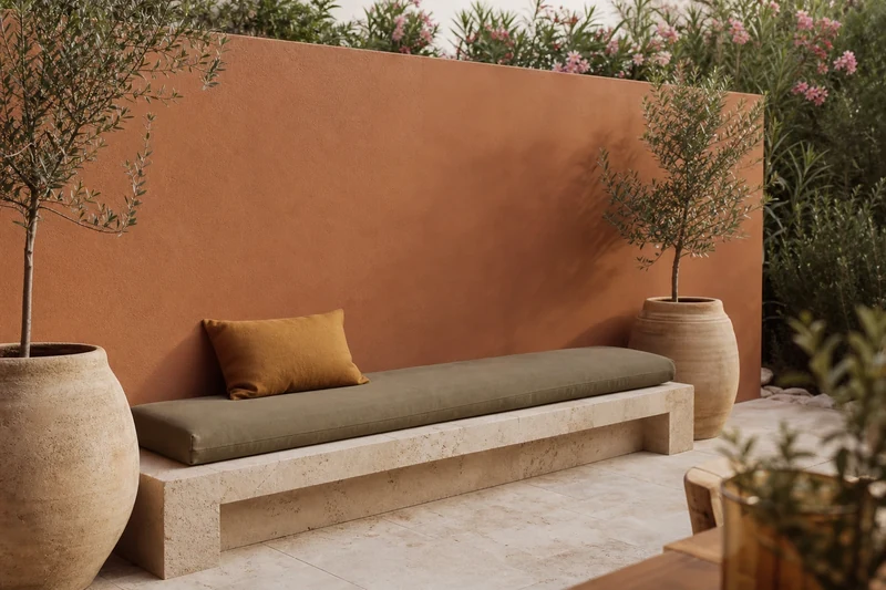 Mur de terrasse en terracotta avec oliviers en pots sable et banc en pierre claire