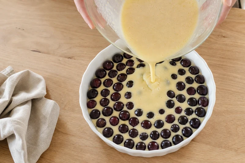 Versement de l'appareil à clafoutis sur les cerises non dénoyautées dans un moule blanc
