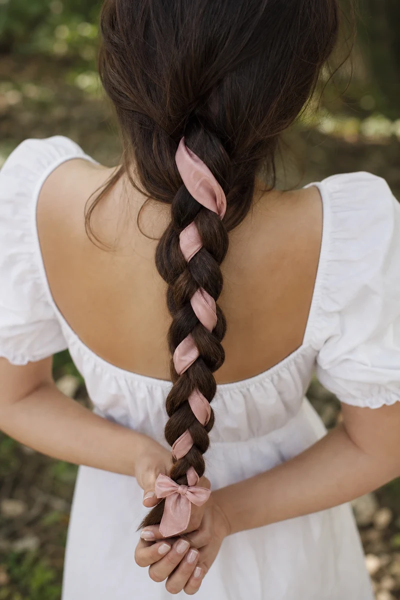 Tresse longue châtain foncé entrelacée d'un ruban de soie rose poudré