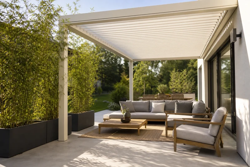 Pergola bioclimatique aluminium blanche avec lames semi-ouvertes au-dessus d'un salon teck